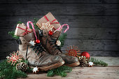 Old hiking boots filled with sweets, gifts and Christmas decoration on Nicholas day, or German Nikolaus Tag, on the 6th December it is tradition to put the shoes outside, rustic wooden background with copy space