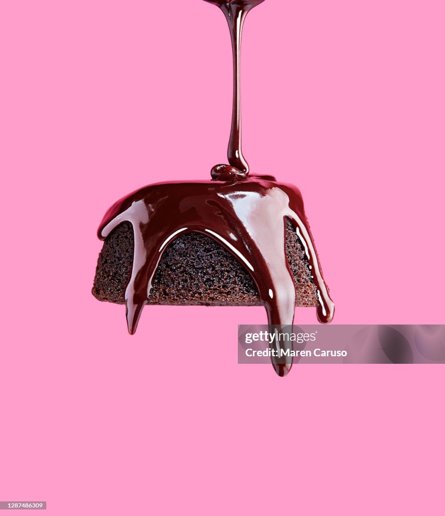 Chocolate frosting being poured onto chocolate cake with pink background