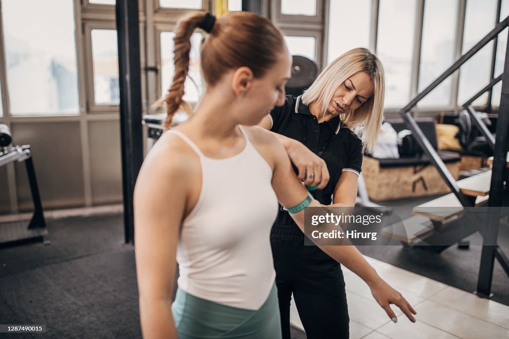 Joven entrenador personal mujer que mide los brazos de la mujer en el gimnasio