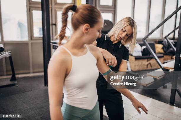 joven entrenador personal mujer que mide los brazos de la mujer en el gimnasio - composición fotografías e imágenes de stock