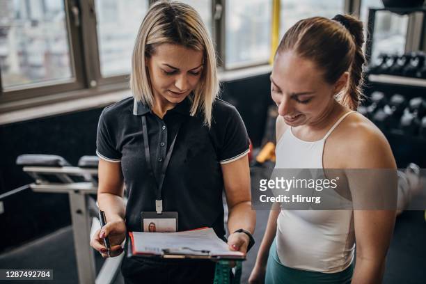 young fit sportswoman talking with her personal trainer in the gym - coach clipboard stock pictures, royalty-free photos & images