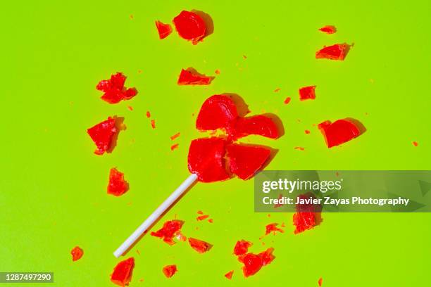 broken red heart-shaped lollipop on green background - candy heart stock pictures, royalty-free photos & images