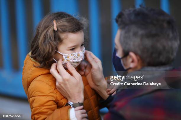 a father putting a protective face mask on his little daughter in front of school - child coronavirus sick stock pictures, royalty-free photos & images