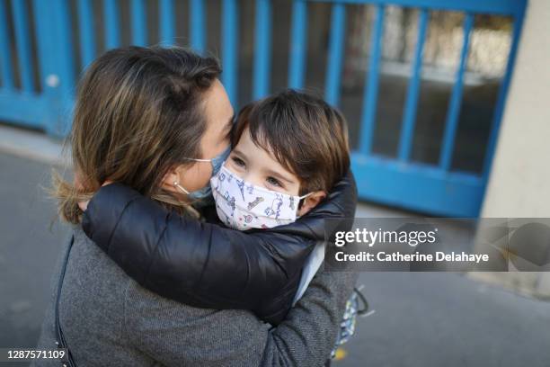 a little boy wearing a protective face mask, embracing his mother in front of school - epidemic school stock pictures, royalty-free photos & images