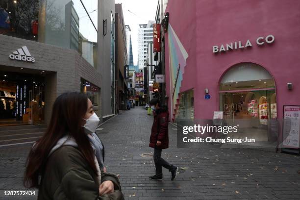 People wearing masks to prevent the spread of coronavirus walk along the nearly empty Myeongdong shopping district on November 25, 2020 in Seoul,...