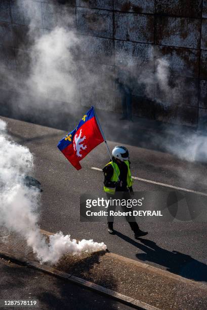 Manifestant au milieu de gaz lacrymogène portant un drapeau de la Ville de Lyon lors de la manifestation des Gilets jaunes le 23 février 2019 à Lyon,...