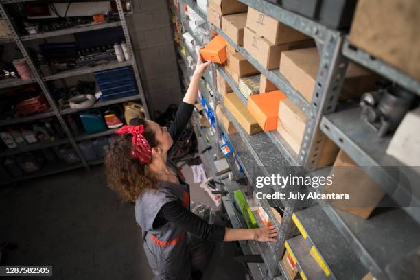 woman in workshop looks for spare parts and pieces in different boxes placed on the shelves - car spare parts stock pictures, royalty-free photos & images