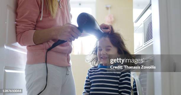 mother blow cold air with a hair dryer to her three year old son - brushing photos et images de collection