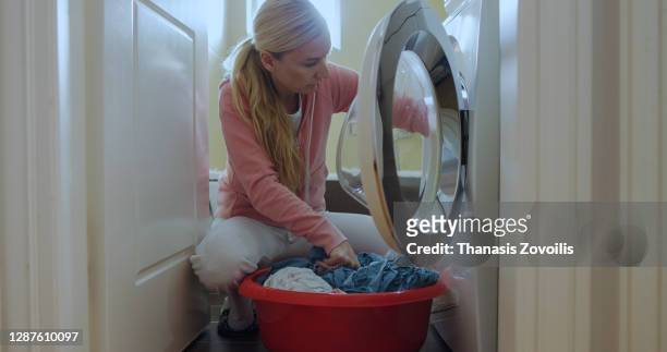young woman putting laundry in a washing machine - laundry woman stock pictures, royalty-free photos & images