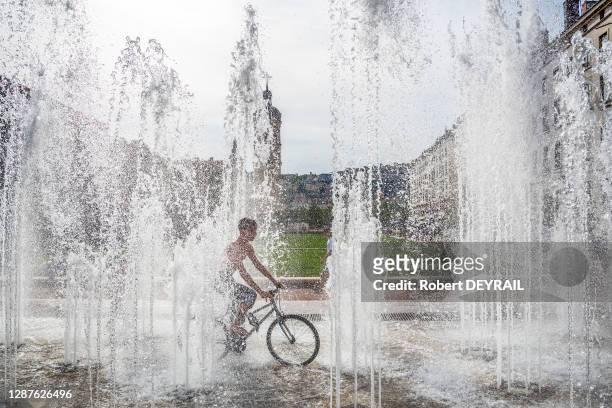 Un enfant avec un vélo profite de la fraicheur des jets d'eau de la place Bellecour lors de la canicule le 25 Juin 2019 à Lyon, France