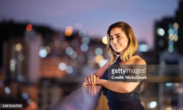 lächelnde junge frau lehnt sich auf einem balkon geländer in der dämmerung - evening gown stock-fotos und bilder