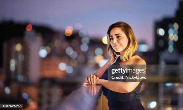 joven sonriente apoyada en un balcón barandilla al atardecer - evening wear fotografías e imágenes de stock