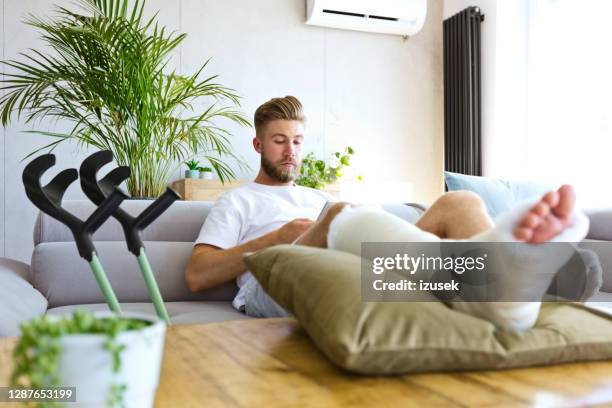 joven con la pierna rota usando el teléfono inteligente - pierna fracturada fotografías e imágenes de stock