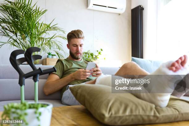 young man with broken leg using smart phone - broken leg stock pictures, royalty-free photos & images