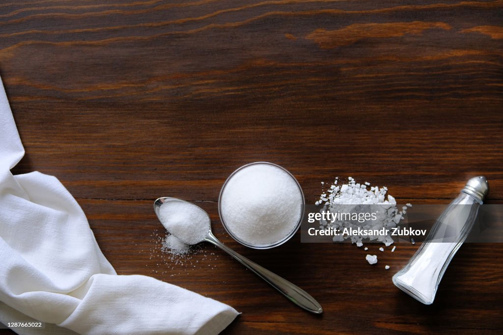 Natural, organic, sea, white salt in a spoon, in a Cup, in a salt shaker, poured on a wooden table. Next to the linen towel. The concept of cooking healthy food, cosmetology. Selective focus