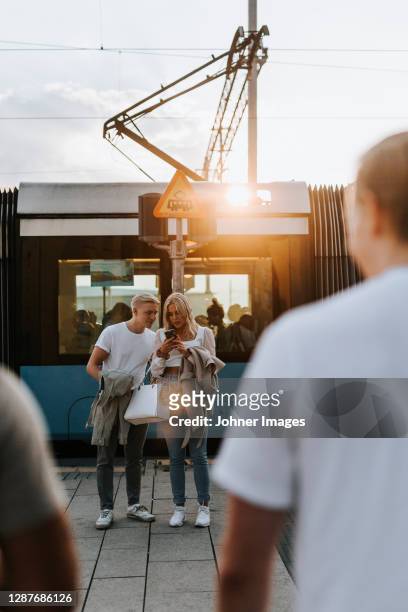 young friends checking cell phone at train crossing - gothenburg stock-fotos und bilder