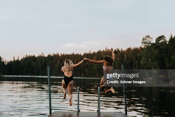 women jumping together into water - jumping into lake stock-fotos und bilder