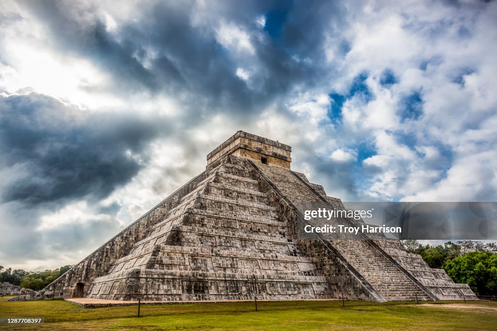 Kukulkan pyramid at Chichen Itza archaeological site against dramatic sky.
