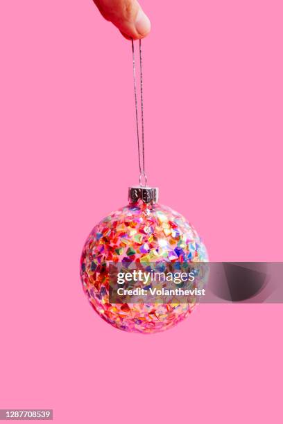 fingers holding a bright and colorful christmas tree ball on pink background - christmas background no people stock pictures, royalty-free photos & images