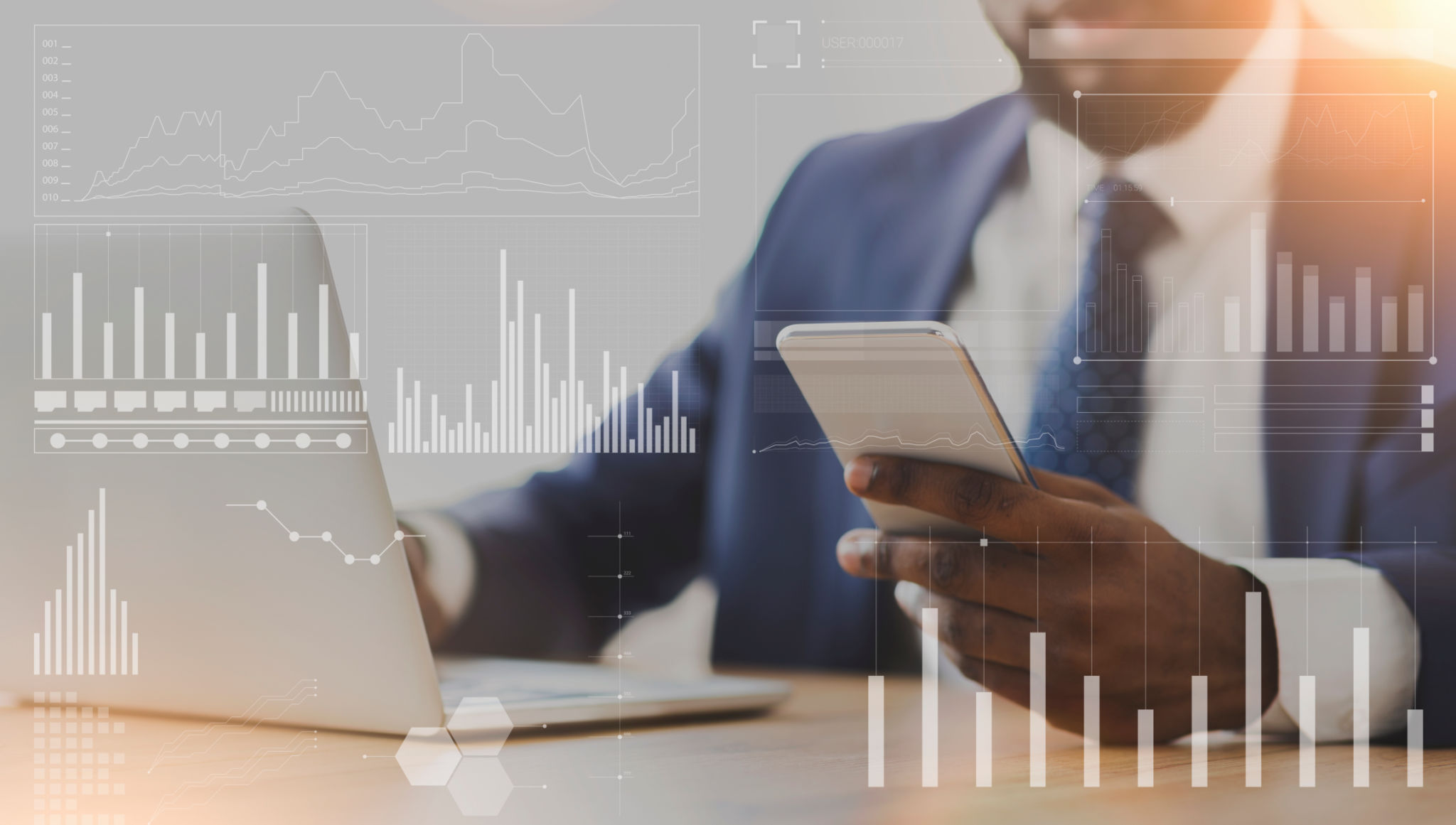 African American businessman using cellphone and laptop at workplace, collage with company analytics on imaginary screen African American businessman using cellphone and laptop at workplace, collage with company analytics on imaginary screen