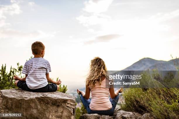 young woman and boy preforms yoga in mountains at sunset - back shot position stock pictures, royalty-free photos & images