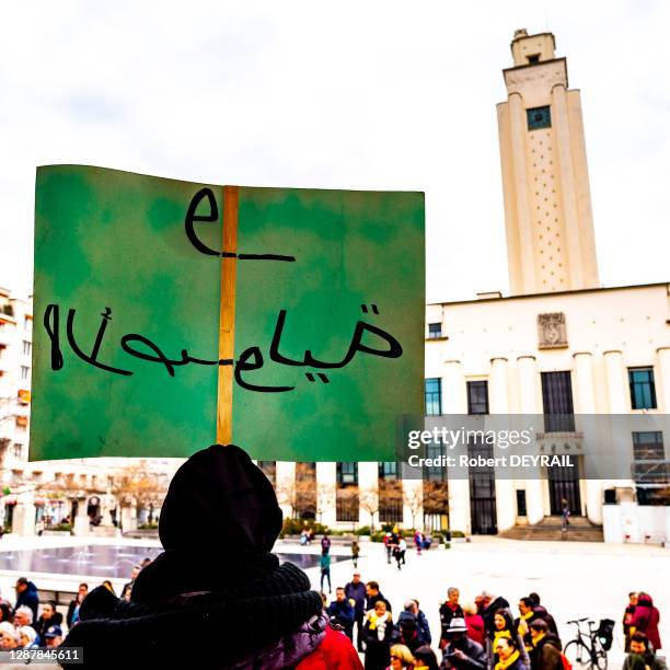 Pancarte portée par une femme voilée et calligraphiée en arabe lors d'un rassemblement de femmes sur les marches de la mairie pour lutter contre les...
