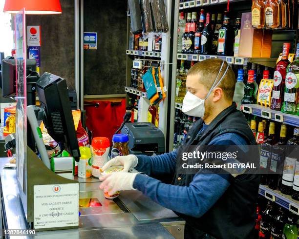 Caissier d'un supermarché avec un masque et des gants de protection enregistrant des produits lors du quatrième jour du confinement le 20 mars 2020 à...