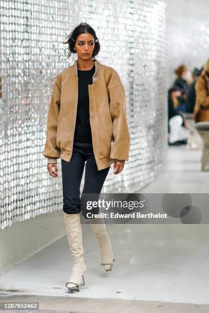 Model wears hair clips, a beige oversized teddy suede jacket, a black pullover, black pants, white high boots, outside Paco Rabanne, during Paris...