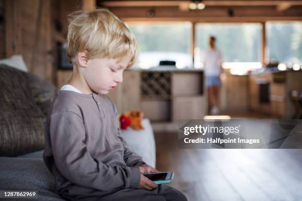 small boy sitting indoors on holiday, using smartphone. - parental control stock-fotos und bilder