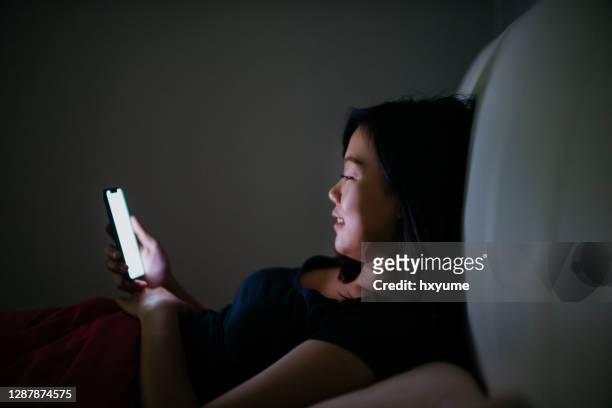 jeune femme asiatique utilisant le smartphone dans l’obscurité - ignorance photos et images de collection