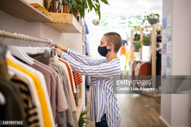 saleswoman with face mask arranging clothes in store - vestido a rayas fotografías e imágenes de stock