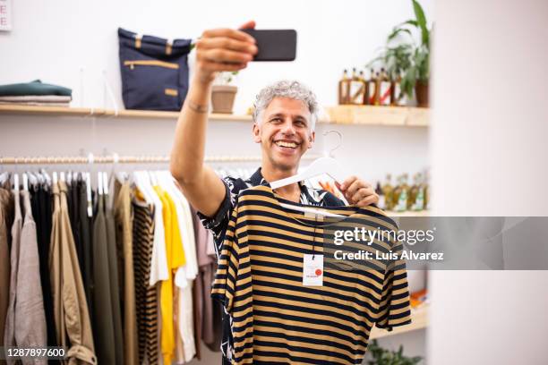 smiling male customer taking selfie holding a t-shirt - kledingstuk stockfoto's en -beelden