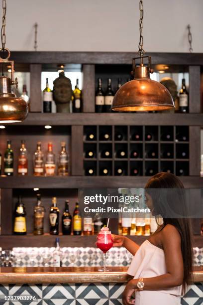 young african woman enjoying a strawberry daiquiri at bar counter - daiquiri stock pictures, royalty-free photos & images