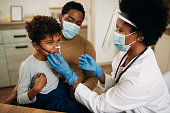 Small black boy receiving asthma treatment while doctor is vising him at home due to COVID-19 pandemic.