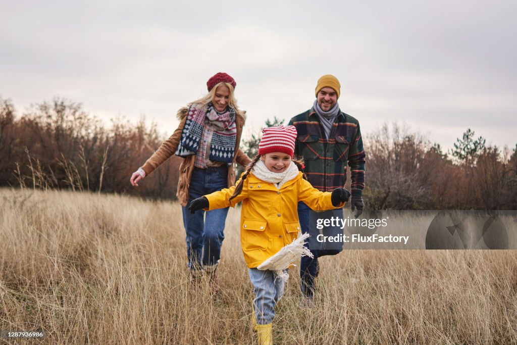 Fröhliche Tochter läuft an einem Weihnachtsmorgen mit ihren Eltern durch die Wiese