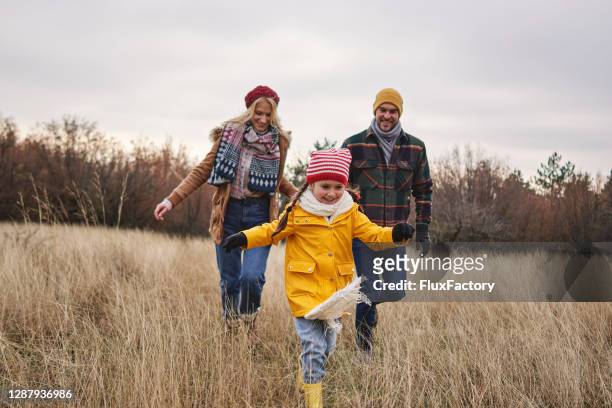 cheerful daughter running through meadow during hike with her parents on a christmas morning - winter stock pictures, royalty-free photos & images