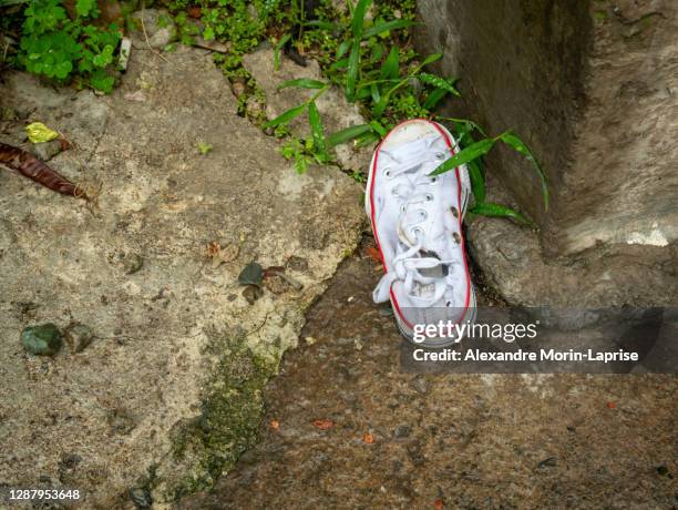 an old white sports shoe lying in the street - lost item stock-fotos und bilder