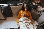 Young woman lying on sofa and using cell phone at home