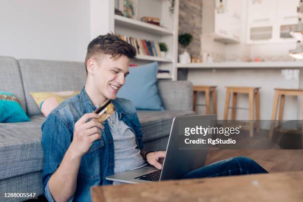 young man buying something online from home - young men shopping stock pictures, royalty-free photos & images