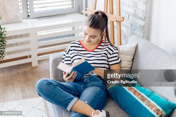 chica relajándose en el sofá y leyendo su novela favorita - reading fotografías e imágenes de stock