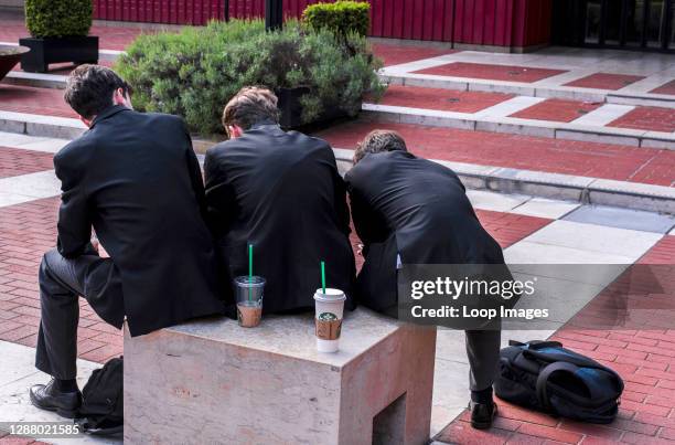 Boys in their school uniform and a rucksack on the floor are seen from behind creating a strange sloping shape in the gardens of the British Library.