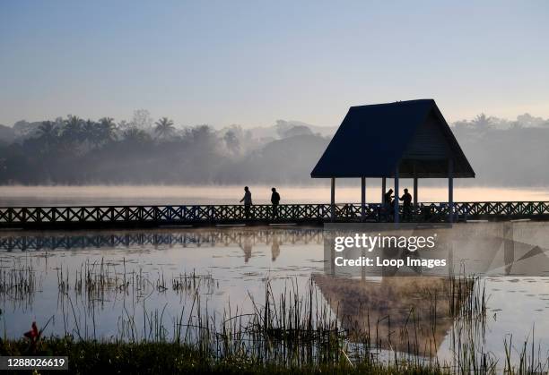 Figures are silhouetted against dawn mist rising at a lake in Loikaw in Myanmar.