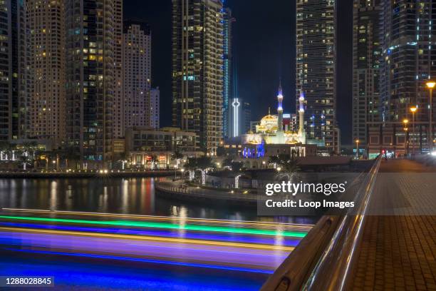 Dhow dinner cruise leaves trails of colourful light beneath an iconic waterfront Mosque in the Dubai Marina.