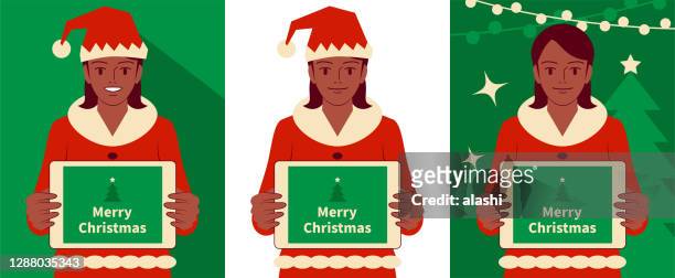 smiling beautiful teenage girl dressed in a santa claus suit holding a digital tablet of blank screen and looking at camera - ethnic woman at christmas stock illustrations