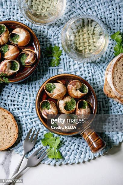 Escargots de Bourgogne - Snails with herbs butter. Gourmet dish. In traditional ceramic pan with coriander. Bread. Glass of white wine on blue napkin...