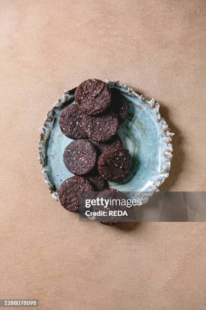 Homemade dark chocolate salted brownies cookies with salt flakes in blue ceramic plate over brown texture background. Flat lay. Space.