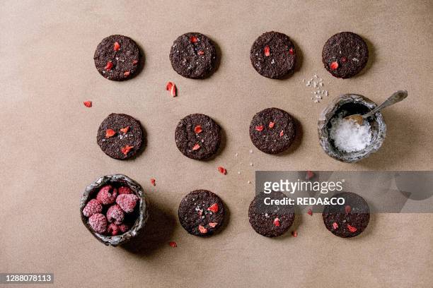 Homemade dark chocolate salted brownies cookies decorated by dried raspberries. Served with salt flakes. Frozen berries over brown texture...