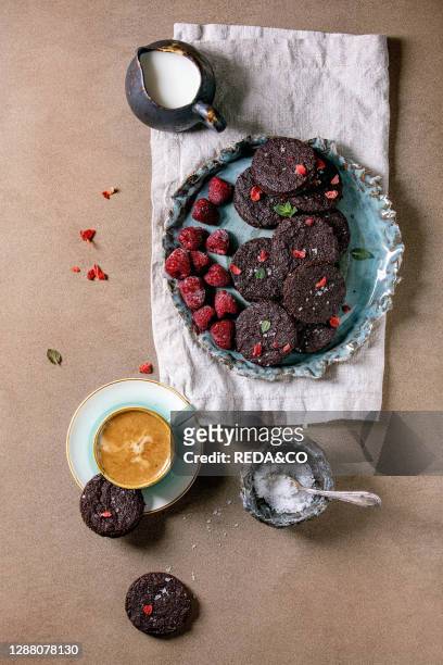 Homemade dark chocolate salted brownies cookies decorated by dry and fresh raspberries. Served with salt flakes. Berries. Mint. Milk and cup of...