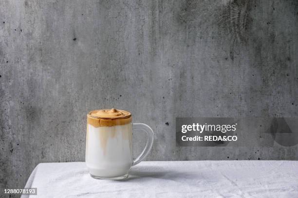 Dalgona frothy coffee trend korean drink milk latte with coffee foam in glass mug standing on white cotton table cloth. Copy space.