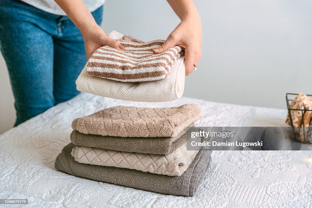 Woman folding stack of fresh laundry and towels, organizing laundry in boxes and baskets.